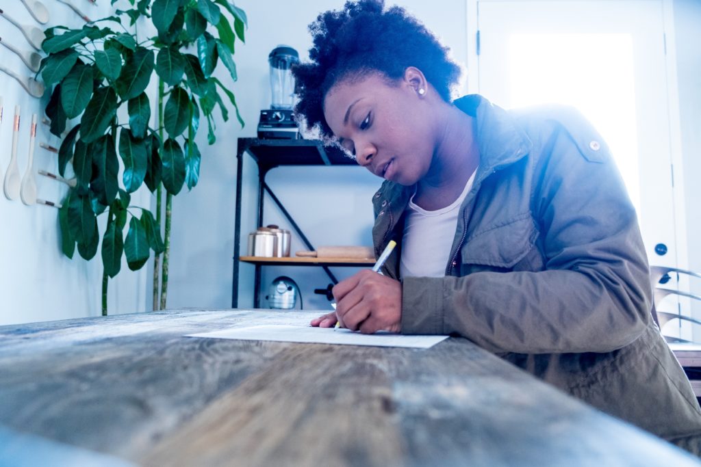 Millennial female black woman fills out a form at a table.