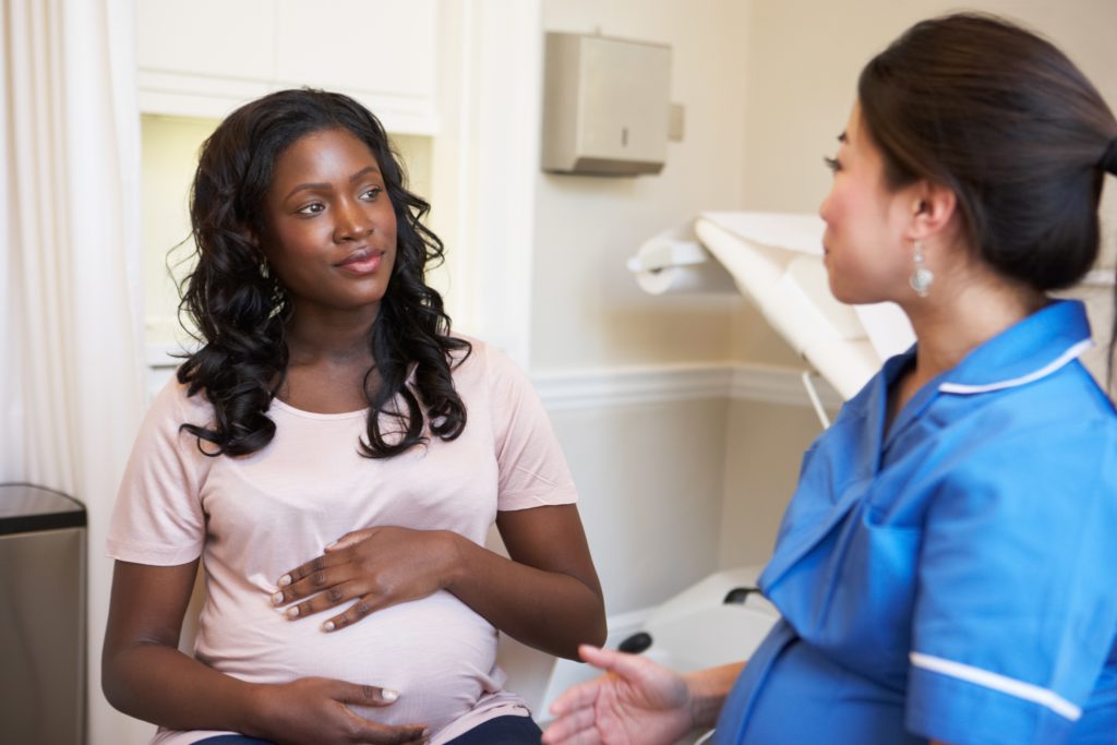 Pregnant woman meeting with nurse in clinic to discuss pregnancy