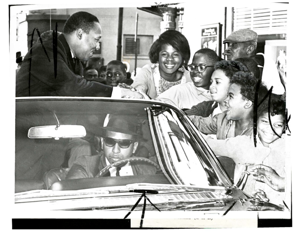 Dr. Martin Luther King, Jr. leaning out of a car and shaking kids' hands.