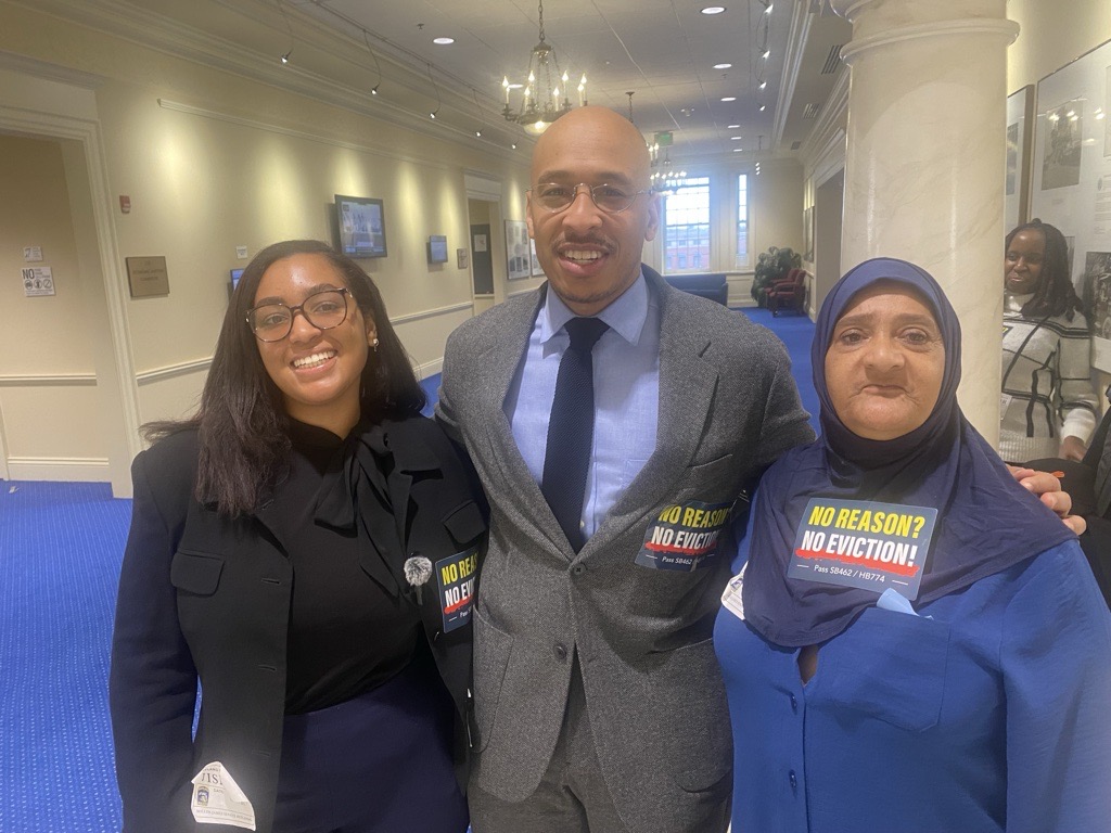 Three people standing together in the halls of the Maryland General Assembly, wearing stickers that say No Reason? No Eviction!