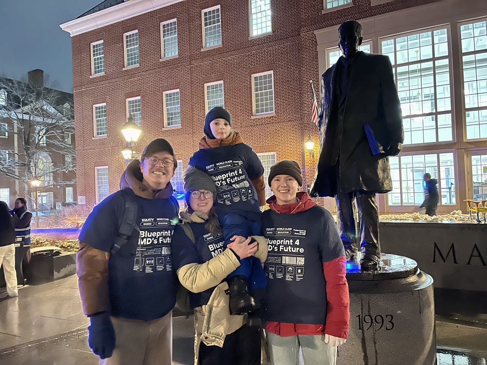 Group of three adults and a child at night standing next to a statue